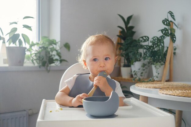 Un bambino che fa i suoi primi tentativi di mangiare da solo Un bambino nel seggiolone con in mano un cucchiaio e che mangia