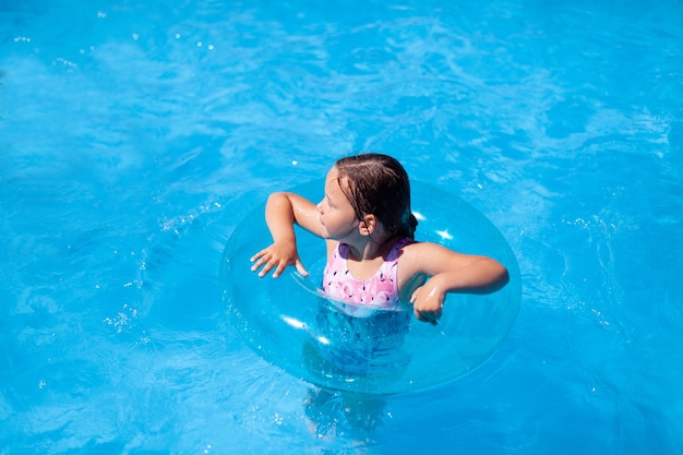 Un bambino che impara a nuotare è tenuto per sicurezza da un cerchio gonfiabile trasparente blu nel mare il c...