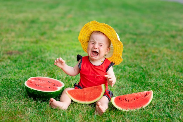 Un bambino che piange in estate sull'erba verde mangia un'anguria, spazio per il testo