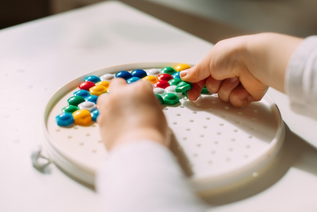 Un bambino con entrambe le mani dispone un mosaico colorato in uno stampo di plastica.