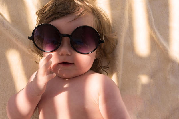 Un bambino con gli occhiali da sole guarda la telecamera in estate al resort