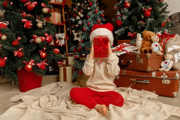 Un bambino con il cappello di Babbo Natale che tiene la confezione regalo rossa che gli copre il viso