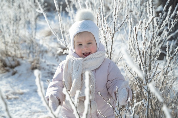 Un bambino con un caldo cappello bianco e sciarpa gioca con la neve mentre cammina nella foresta invernale nevicata magia invernale emozione luminosa proteggendo la pelle dal gelo
