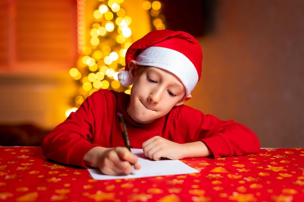 Un bambino con un cappello da Babbo Natale di Capodanno scrive una lettera a Babbo Natale