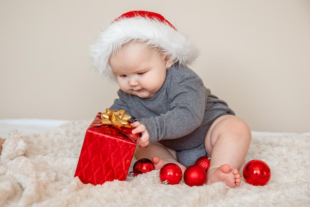 Un bambino con un cappello di Babbo Natale è sdraiato sul letto a giocare con le palle di Natale