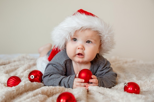 Un bambino con un cappello di Babbo Natale è sdraiato sul letto a giocare con le palle di Natale