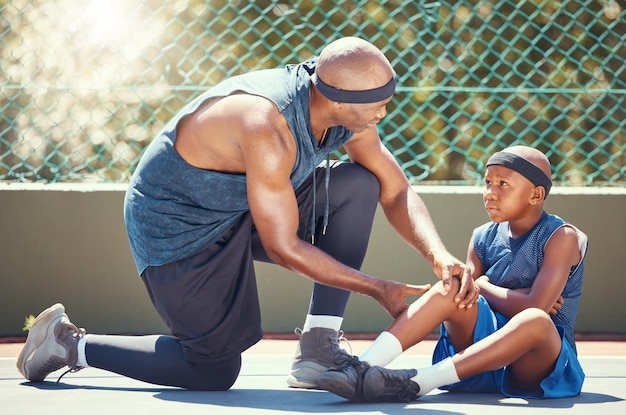 Un bambino con un infortunio al ginocchio da basket con papà ha messo un cerotto di emergenza per un incidente di gioco di allenamento sportivo al campo da basket Padre nero africano e squadra di bambini feriti con dolore alle gambe curativo e cerotto per ferite