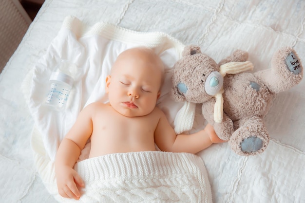 Un bambino con un orsacchiotto dorme in camera da letto su un letto coperto da una coperta bianca