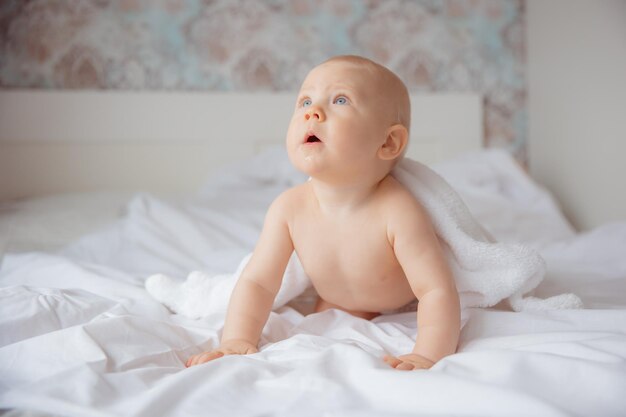 Un bambino con un pannolino è seduto sul letto coperto con un asciugamano dopo il bagno in camera da letto