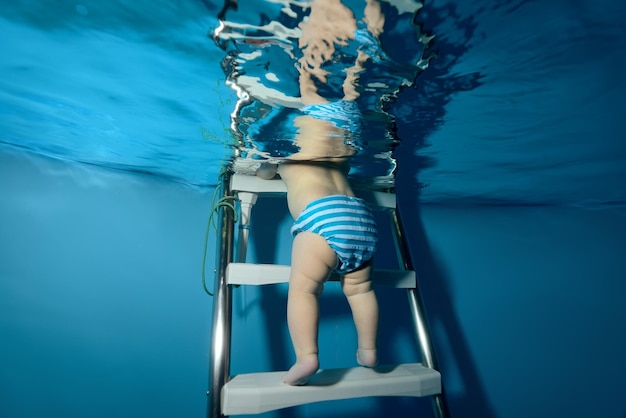 Un bambino con un pannolino scende le scale nell'acqua nella piscina per bambini