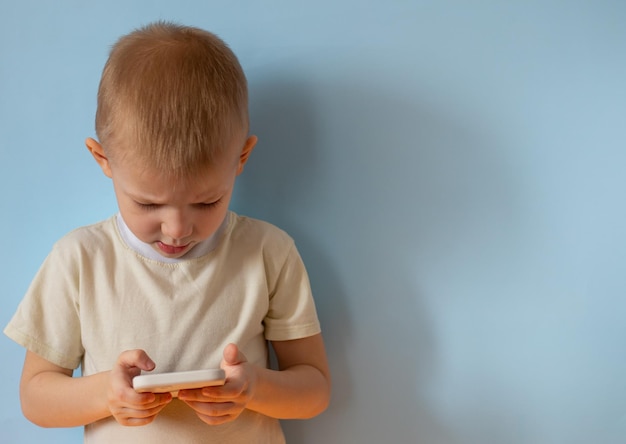 Un bambino con un telefono in mano su sfondo blu in studio Banner copyspace mockup