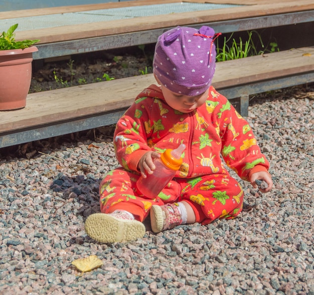 Un bambino con una bottiglia di bevanda seduto sugli scogli in una giornata estiva.