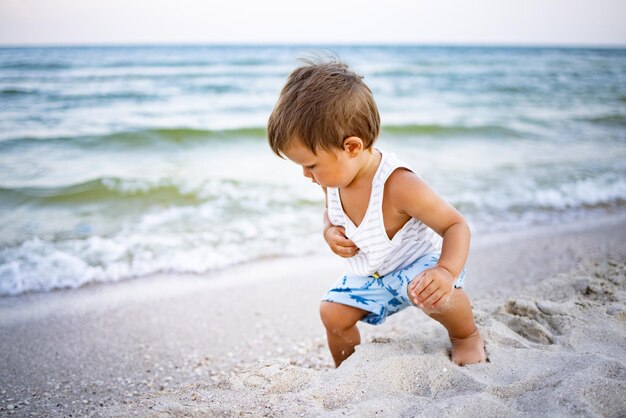 Un bambino con una maglietta a righe raccoglie ciottoli e conchiglie sulla costa in una sera d'estate