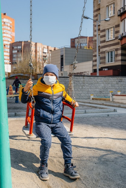 Un bambino con una maschera cammina nel parco giochi durante la quarantena. Resta a casa.