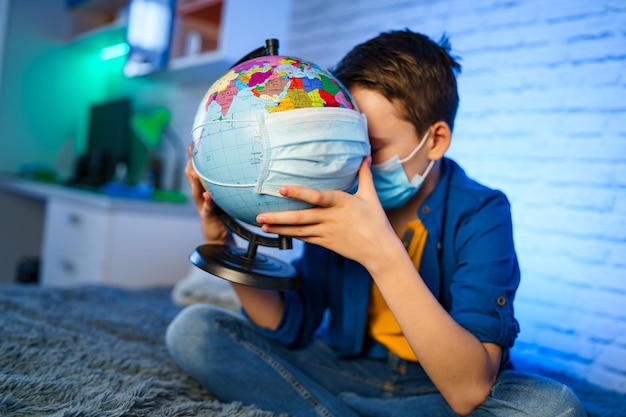 Un bambino con una maschera medica tiene un globo Il ragazzino guarisce il pianeta Concetto di inquinamento dell'aria e dell'ambiente