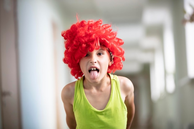 Un bambino con una parrucca brillante Ragazzo divertente con capelli artificiali rossi L'uomo cattivo mostra la lingua