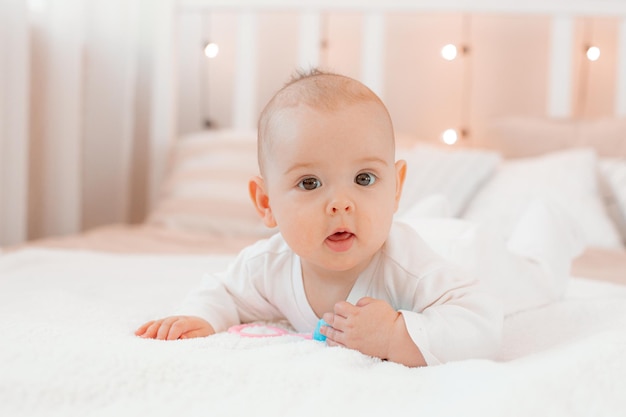 Un bambino con una tuta bianca è sdraiato su un letto con un sonaglio a casa