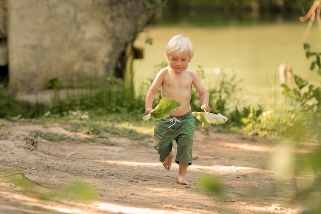 Un bambino di 4 anni a piedi nudi in pantaloncini corre lungo un sentiero nel bosco vicino al fiume.