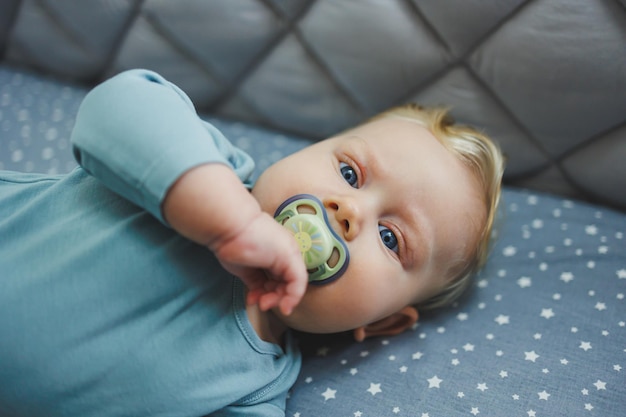 Un bambino di 6 mesi giace in una culla e guarda la telecamera Lenzuola grigia per un letto per bambini