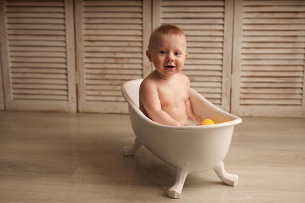 un bambino di 9 mesi sta facendo il bagno in un bagnetto bianco con anatroccoli di gomma