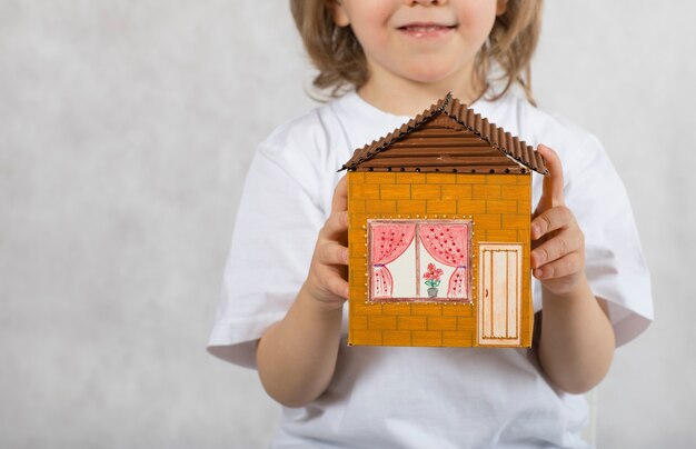 Un bambino di cinque anni tiene una casa di cartone fatta a mano. Avvicinamento