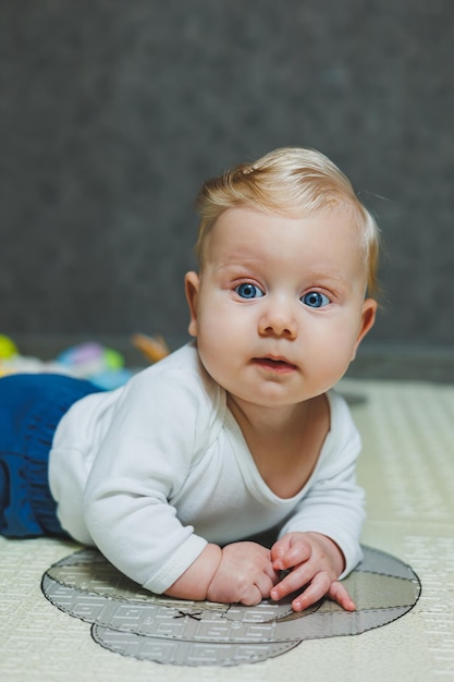 Un bambino di quattro mesi giace sul pavimento su un tappeto e gioca con i giocattoli Il bambino tiene la testa Un bambino impara a strisciare sul pavimento