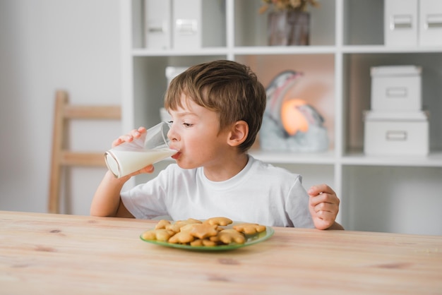 Un bambino di sei anni beve latte con davanti un piatto pieno di biscotti