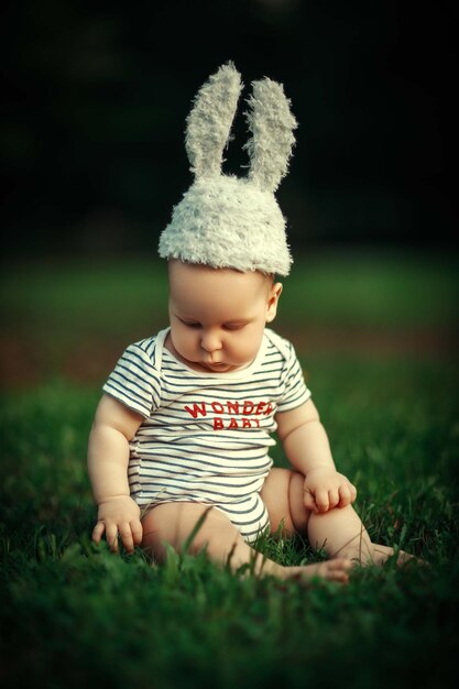 un bambino di sei mesi siede sull'erba alla luce del sole con un cappello da coniglio con belle orecchie