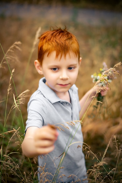 Un bambino di sette anni con i capelli rossi con un mazzo di fiori di campo in estate