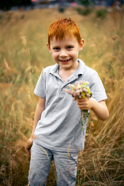 Un bambino di sette anni con i capelli rossi con un mazzo di fiori di campo in estate