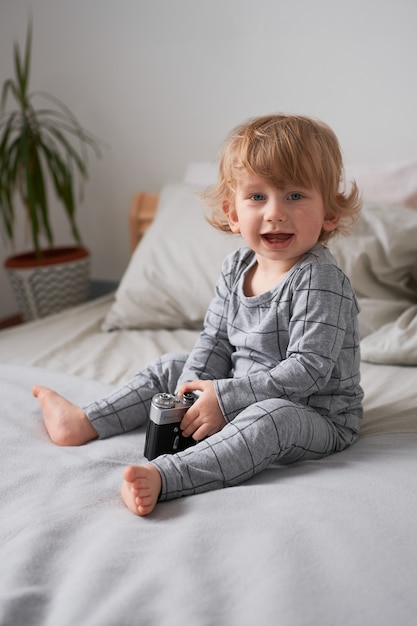 Un bambino di un anno che gioca sul letto con una vecchia macchina fotografica, foto di stile di vita