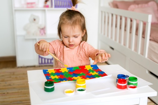 Un bambino di un anno disegna con i colori a guazzo colorando un disegno con puzzle colorati