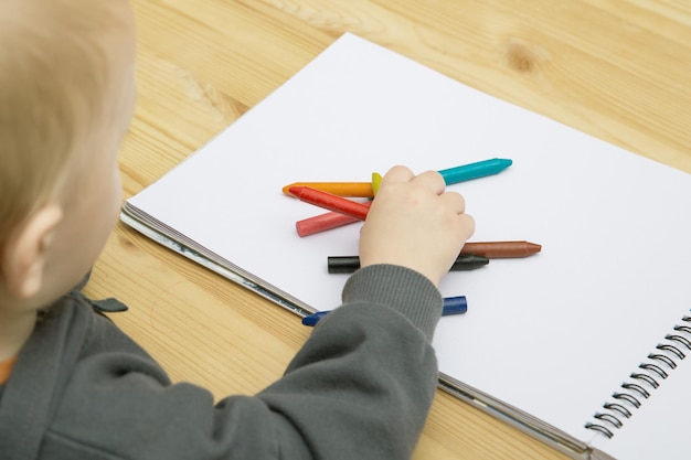 Un bambino disegna con pastelli colorati in un album su un tavolo di legno