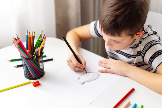 Un bambino disegna su carta bianca con matite colorate mentre è seduto a un tavolo