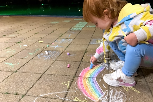 Un bambino disegna un arcobaleno con pastelli multicolori in una sera d'estate fuori dai locali