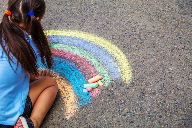 Un bambino disegna un arcobaleno sull'asfalto Messa a fuoco selettiva