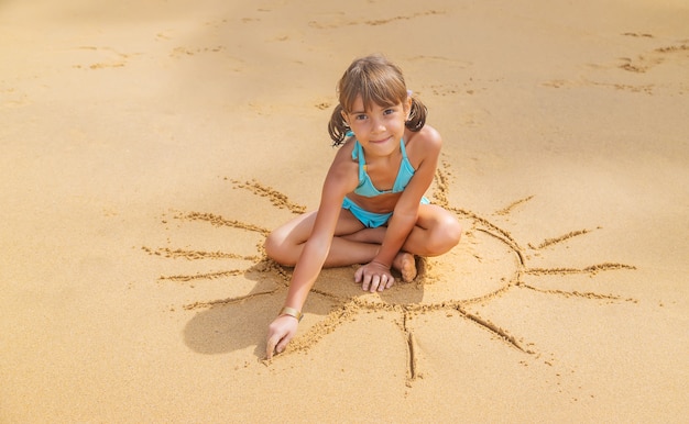 Un bambino disegna un sole sulla spiaggia.