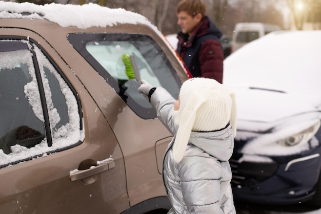 Un bambino e un papà spazzano la neve dall'auto con un pennello dopo una forte nevicata, inverno