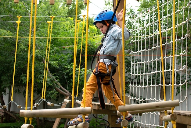 Un bambino felice con casco e attrezzature di protezione si diverte a prendere lezioni nel parco di arrampicata in un giorno d'estate