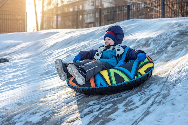 Un bambino felice con sua madre è tubing con un parco da uno scivolo Un divertente weekend invernale nel parco esterno