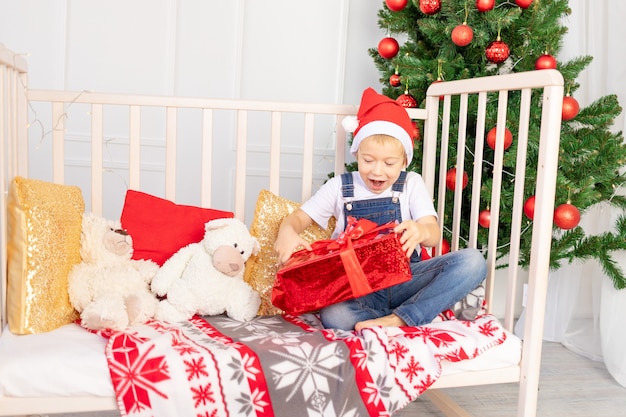 Un bambino felice con un cappello rosso scarta un regalo