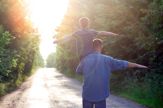 Un bambino felice con un genitore sulle spalle cammina lungo la strada sullo sfondo del parco