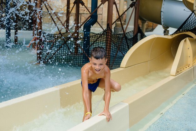 Un bambino felice di sette anni scende dagli scivoli del parco acquatico. Buone vacanze. Vacanze estive e turismo.