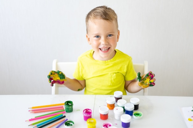 un bambino felice disegna con le dita con colori vivaci sorrisi guarda la telecamera