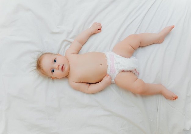 Un bambino felice e gioioso in pannolini è sdraiato su un letto bianco e tiene la sua gamba Posto fotografico di alta qualità per il testo