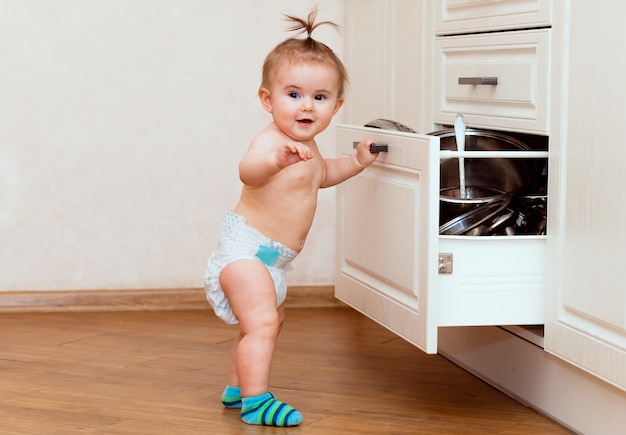 Un bambino felice è in piedi vicino a un armadio aperto in cucina. bambino nella cucina bianca. bambino sorride in una cucina bianca.