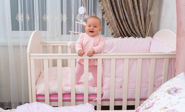 Un bambino felice e ridente nella culla nella scena della camera da letto rosa.