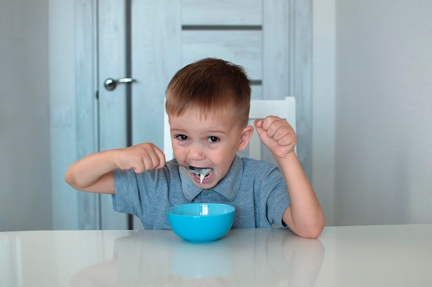 Un bambino felice mangia una sana colazione deliziosa. Ritratto di un bambino che fa colazione. Un bel bambino felice è seduto in cucina e impara con un cucchiaio. Messa a fuoco selettiva.