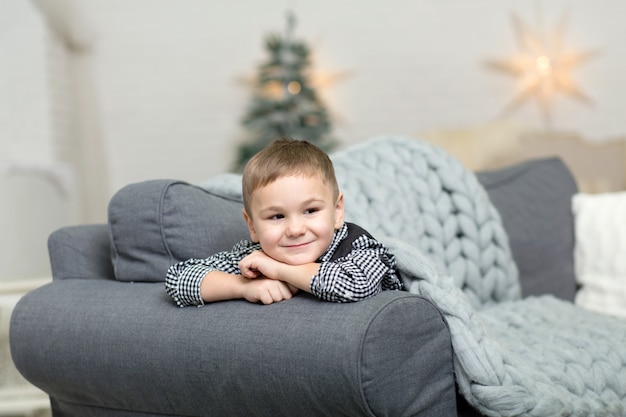 Un bambino giace su un divano coperto da una coperta a maglia grigia e sorride