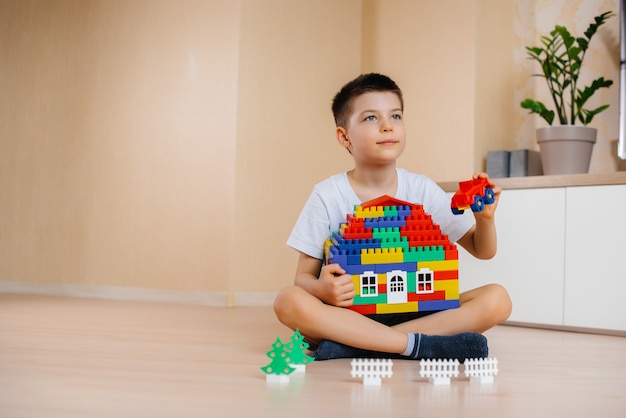 Un bambino gioca con un kit di costruzione e costruisce una grande casa per tutta la famiglia. Costruzione di una casa di famiglia.